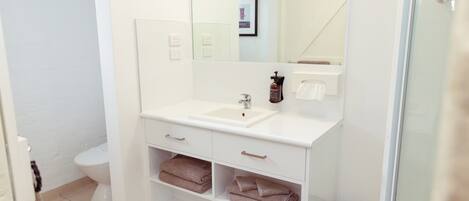 A modern bathroom with a white sink, mirror, and built-in shelves for towels.
