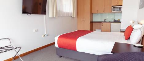 A hotel room with a bed, a TV mounted on the wall, a kitchenette, and a seating area with a sofa and a chair.