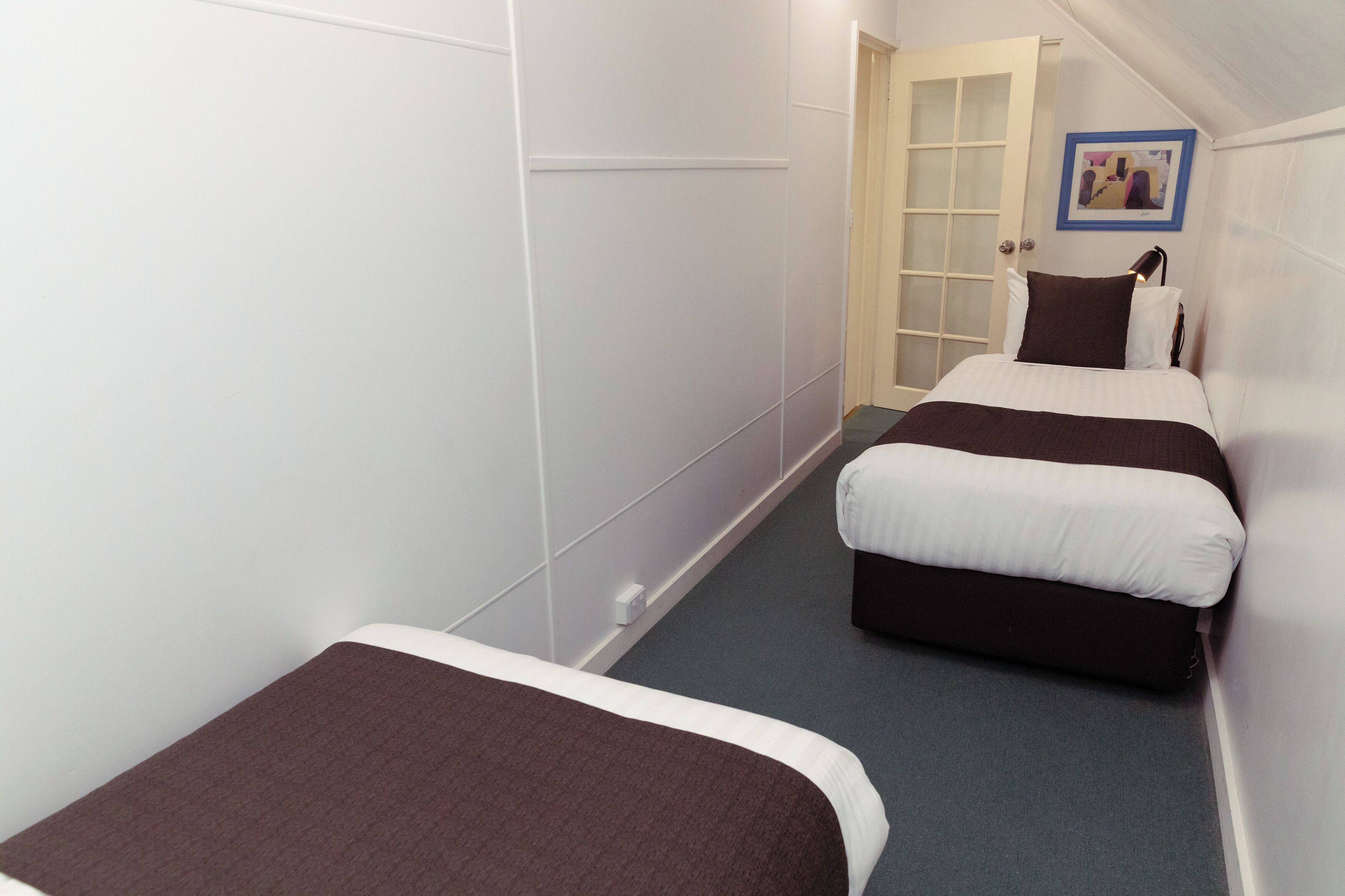 A narrow hallway with two beds, one with a brown and white bedspread and the other with a black and white bedspread.