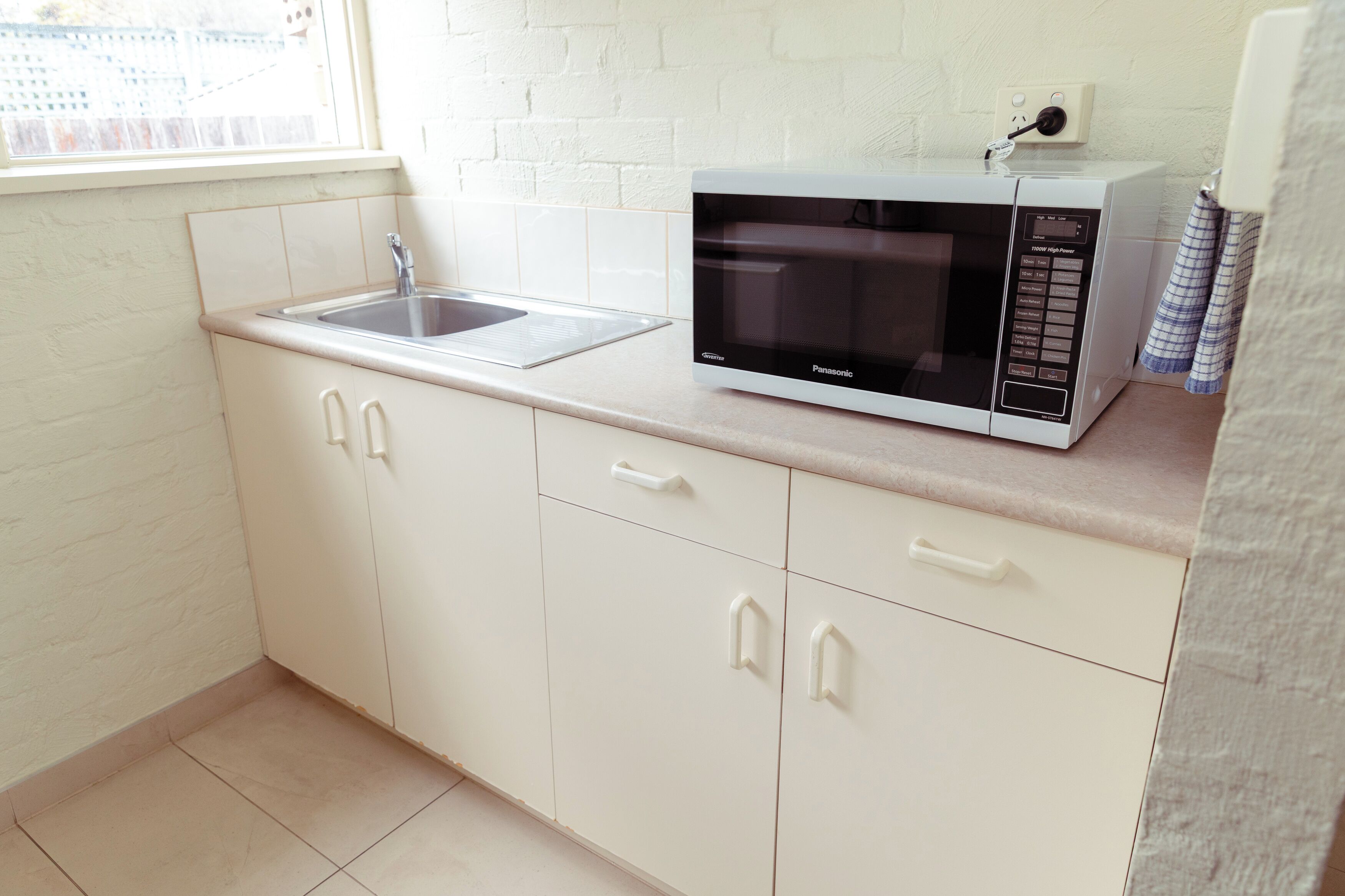 A kitchen with white cabinets, a sink, and a microwave.