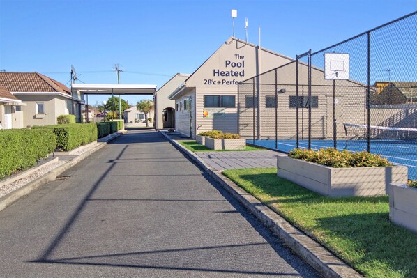 A pathway leading to a building labeled "The Pool Heated 28°C+ Perfect" with a basketball court visible through a fence.