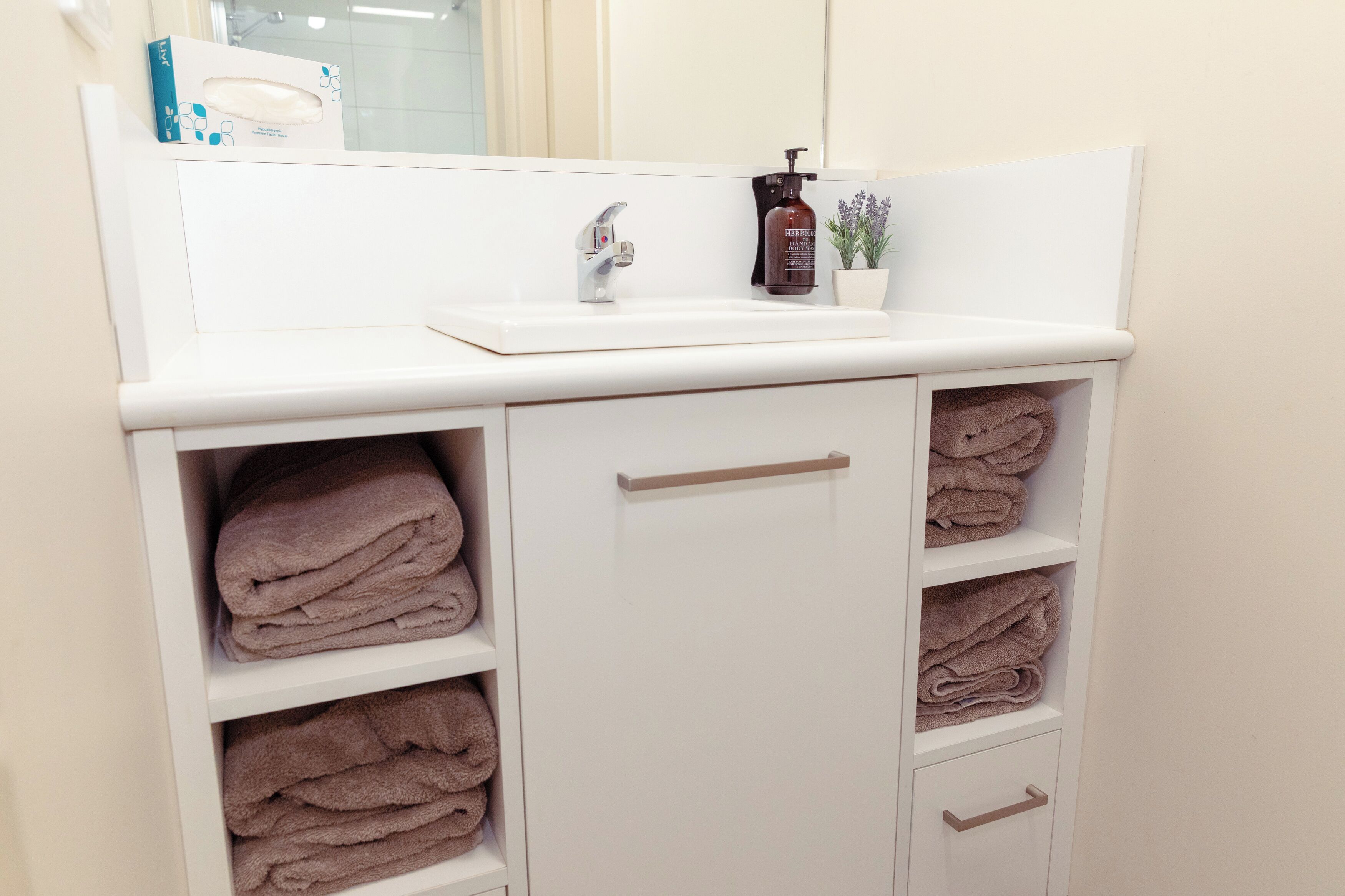 A bathroom with a white sink, a mirror, and a shelf with folded towels.
