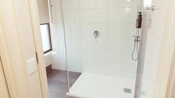 Zona de ducha con mampara de vidrio, pared con azulejos blancos, panel de control y ventana.