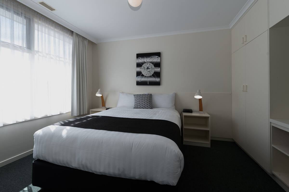 A hotel room with a large bed, bedside lamps, a wall clock, and a wardrobe.