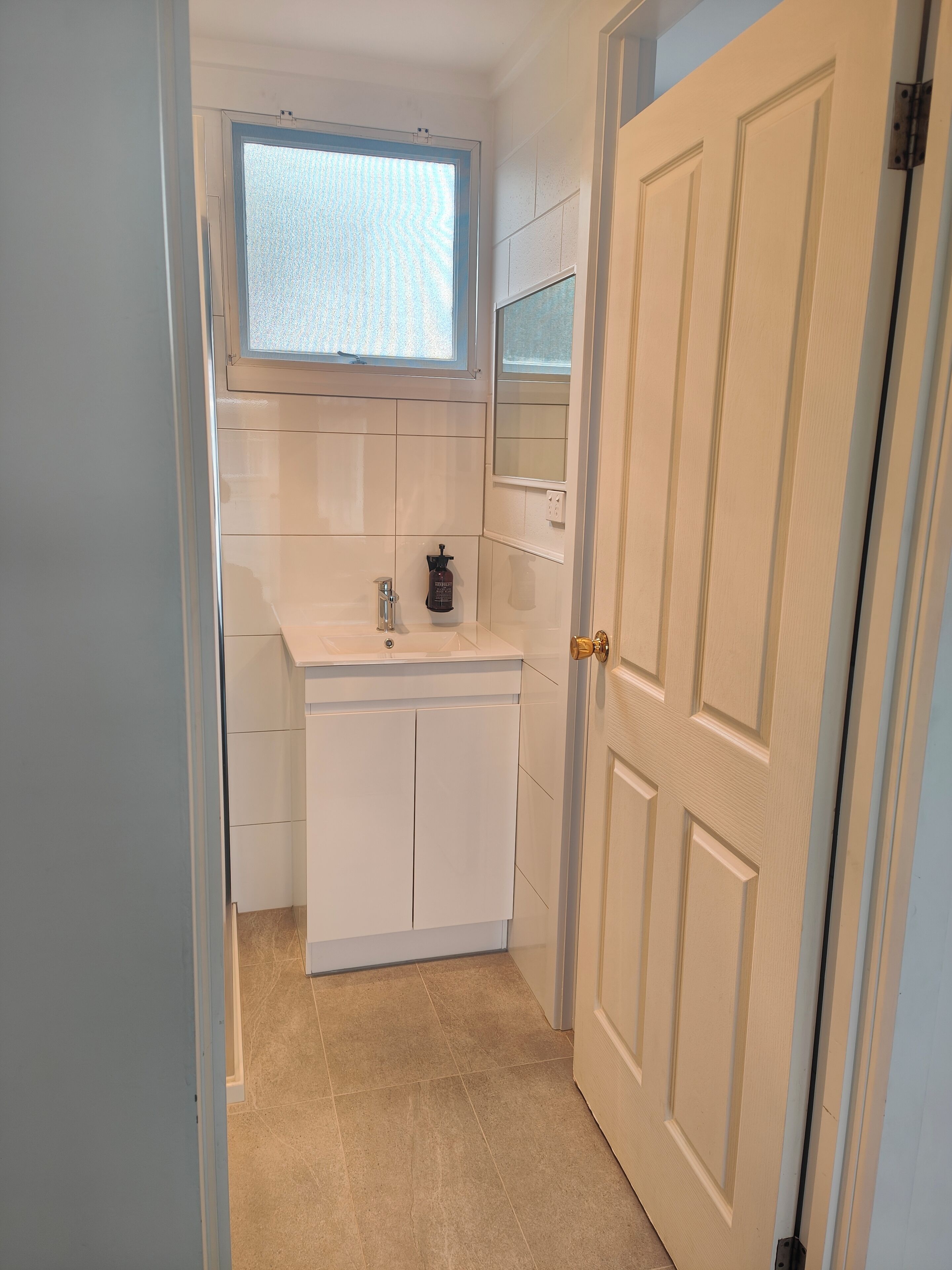 A compact bathroom with a white sink, a mirror, and a window above the mirror.