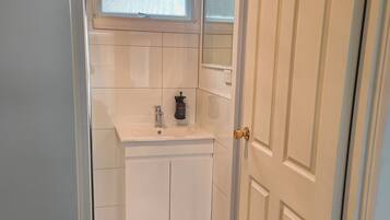 A compact bathroom with a white sink, a mirror, and a window above the mirror.