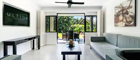 A modern living room with a flat-screen TV, a ceiling fan, a sofa, a coffee table, and a view of the outdoors.