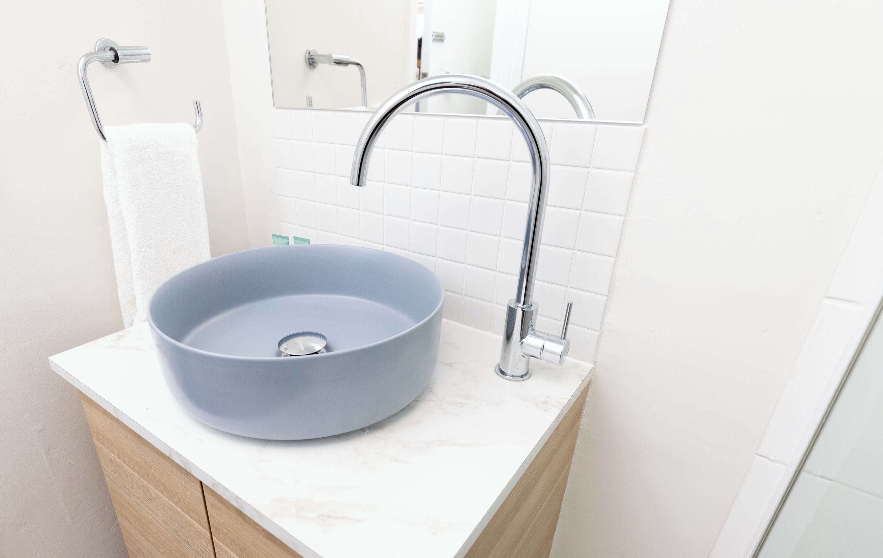 Un baño con un lavamanos azul redondeado, una toalla blanca y un grifo de cromo.
