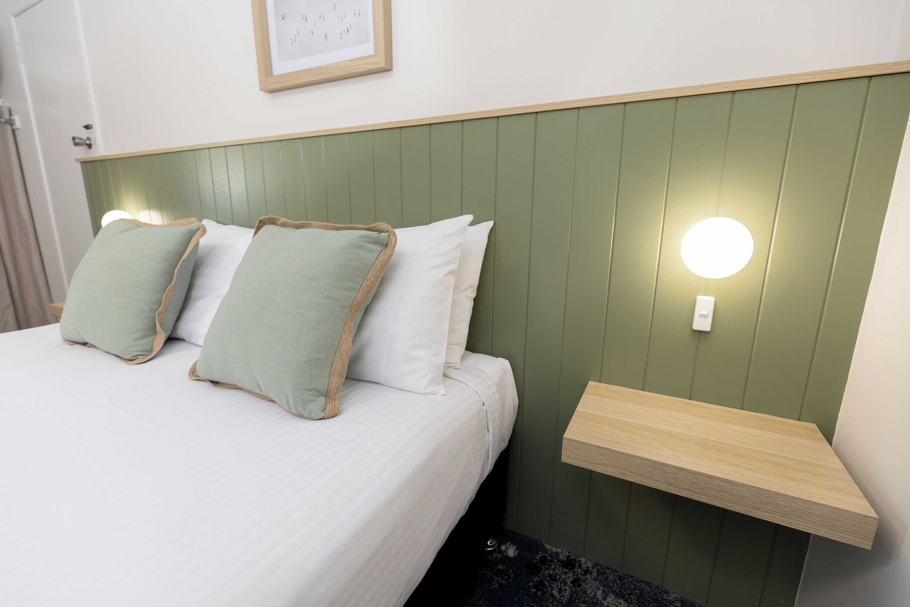 A neatly made bed with two pillows, a bedside table, and a wall-mounted light.