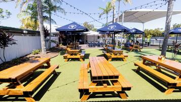 An outdoor seating area with wooden picnic tables and blue umbrellas.