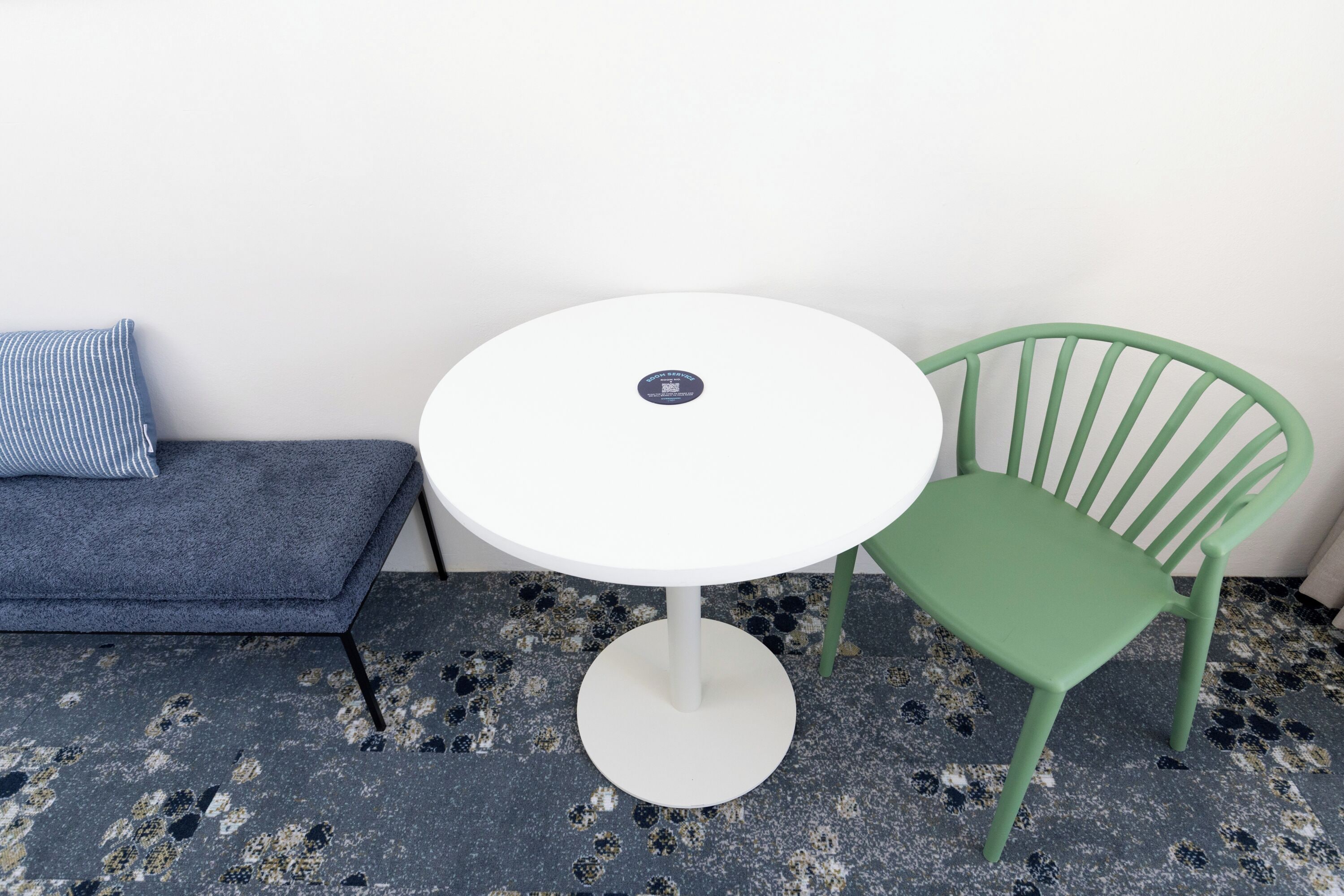 A small room with a white round table, a green chair, and a blue sofa against a white wall.