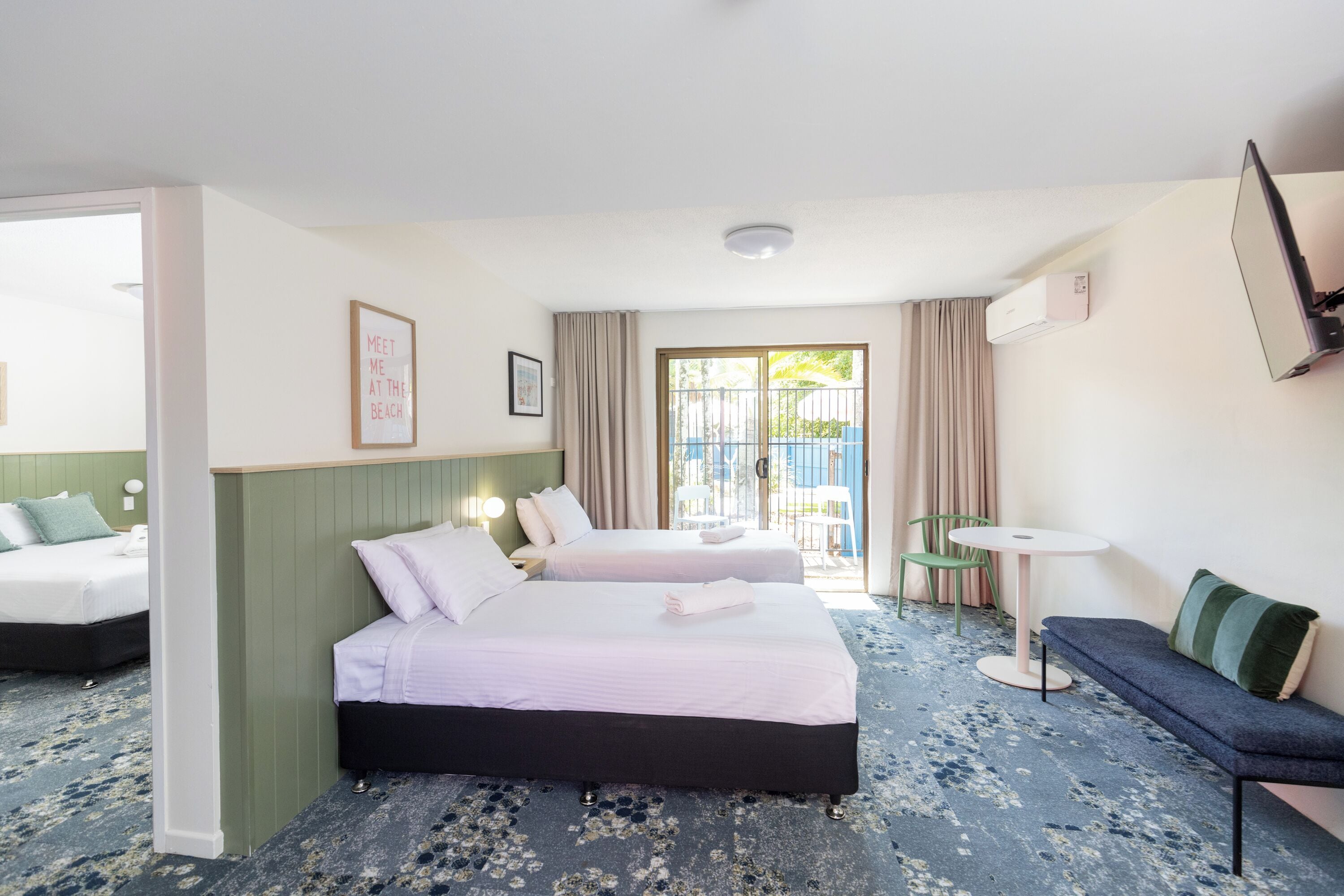 A hotel room with two beds, a sofa, a small table, and a TV.