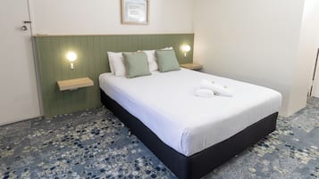 A neatly made bed with white linens and green pillows, a bedside table with a lamp, and a green headboard.