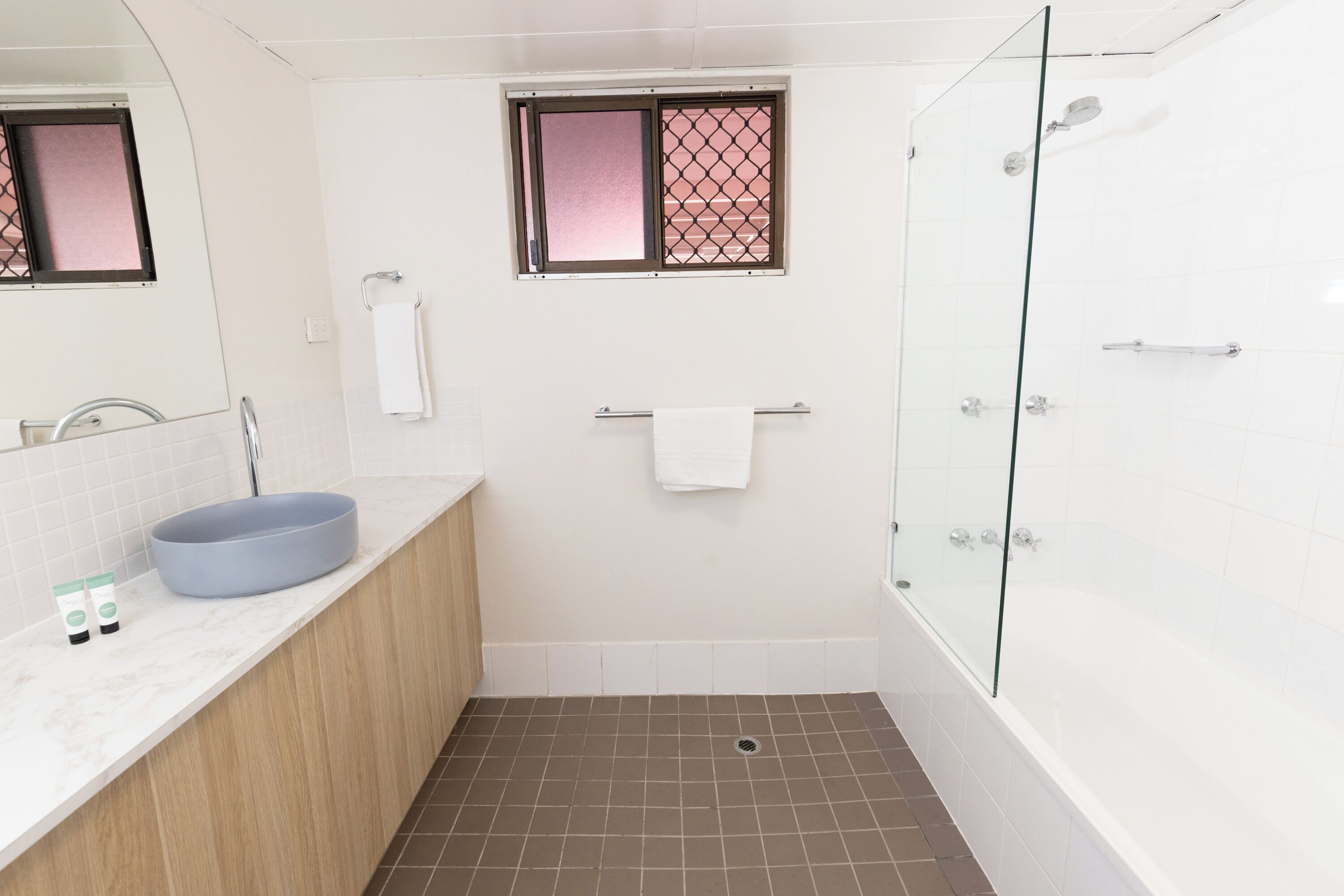 Een badkamer met een bad, een wastafel met een ruime kom, een raam met een metalen hor en een handdoekhouder.