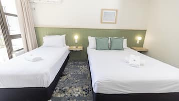 A hotel room with two beds, each with white linens and pillows, a green headboard, bedside lamps, and a framed picture on the wall.