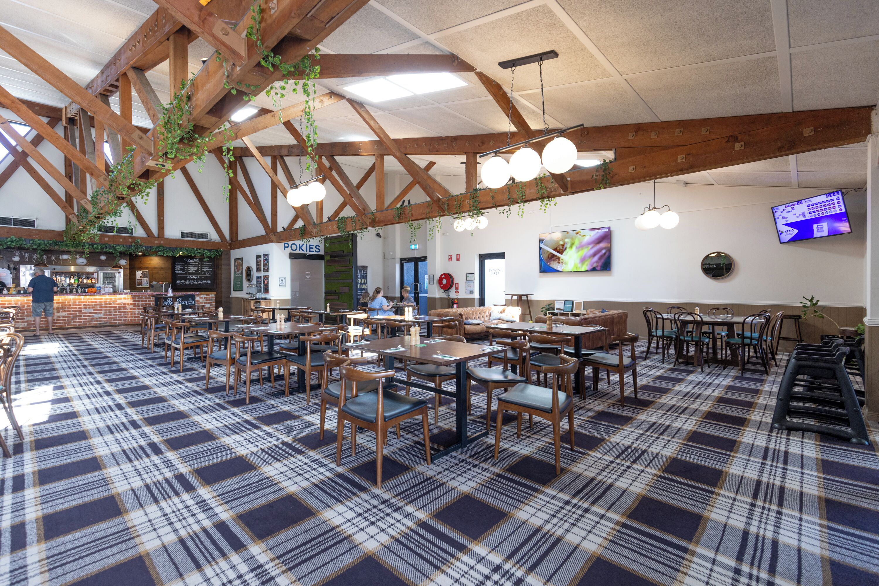 Un restaurante espacioso con suelo a cuadros, vigas de madera, plantas colgantes y una pizarra con el menú.
