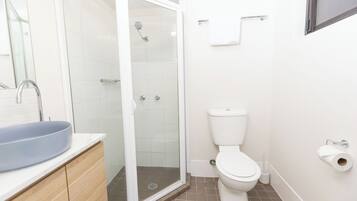 A bathroom with a shower, toilet, sink, and a mirror.