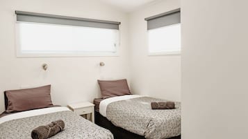 Habitación de hotel con dos camas, cada una con ropa de cama y almohadas estampadas, una mesita de noche pequeña y un ventanal con persiana enrollable.