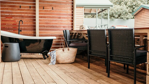 Eine Holzterrasse mit Badewanne, Korbstühlen und Holztisch.