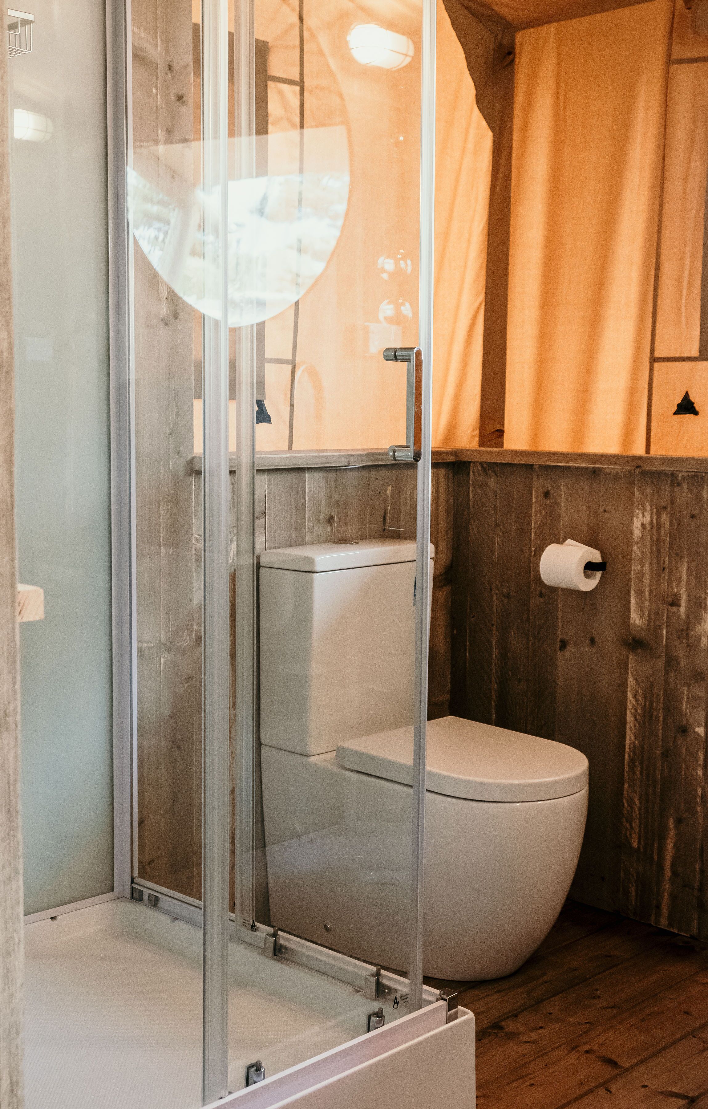 A bathroom with a glass-enclosed shower, a toilet, and a wooden wall.