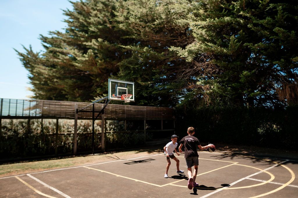 An outdoor basketball court with a hoop, surrounded by trees and a fence.