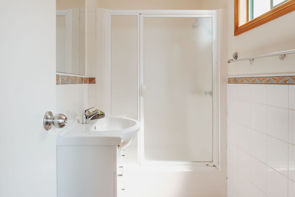 Une salle de bain avec un lavabo blanc, une porte de douche en verre et un mur carrelé agrémenté d’une bordure décorative.
