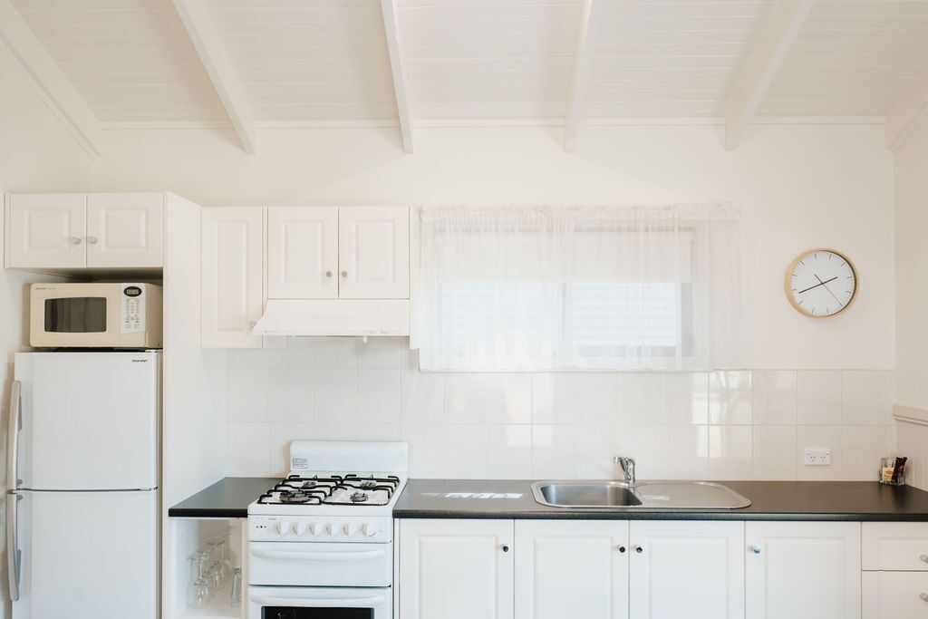 A kitchen with white cabinets, a stove, a microwave, and a sink.