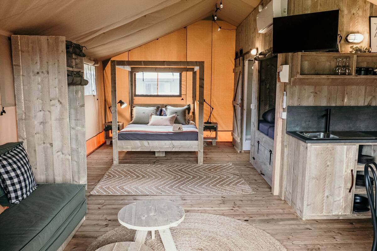 A cozy, wooden interior with a bed, a small table, a sofa, and a kitchenette.