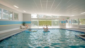 Ein Innenpool mit großen Glaswänden, einer gefliesten Decke und Blick ins Freie.