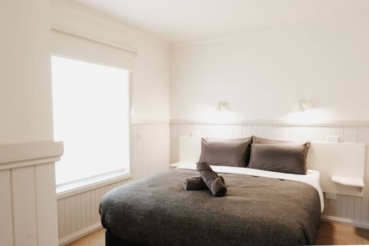 A bedroom with a large window, a bed with a gray blanket, and two wall-mounted lights.