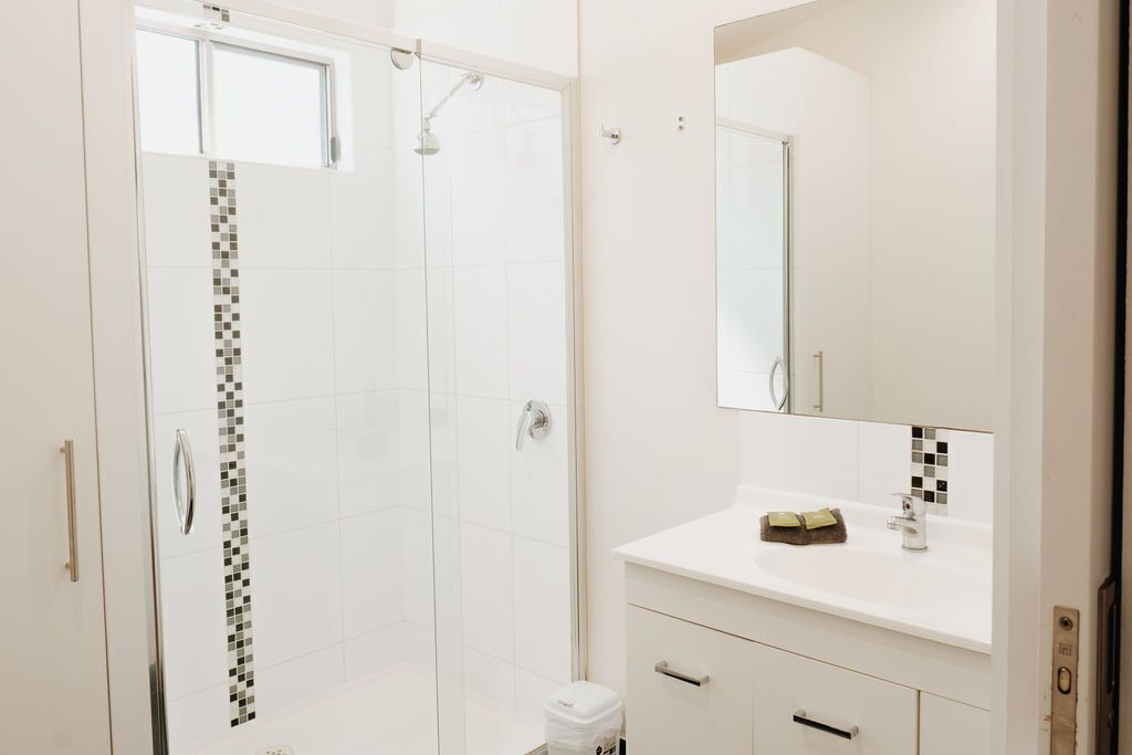 A modern bathroom with a glass-enclosed shower, a white vanity with a mirror, and a tiled backsplash.
