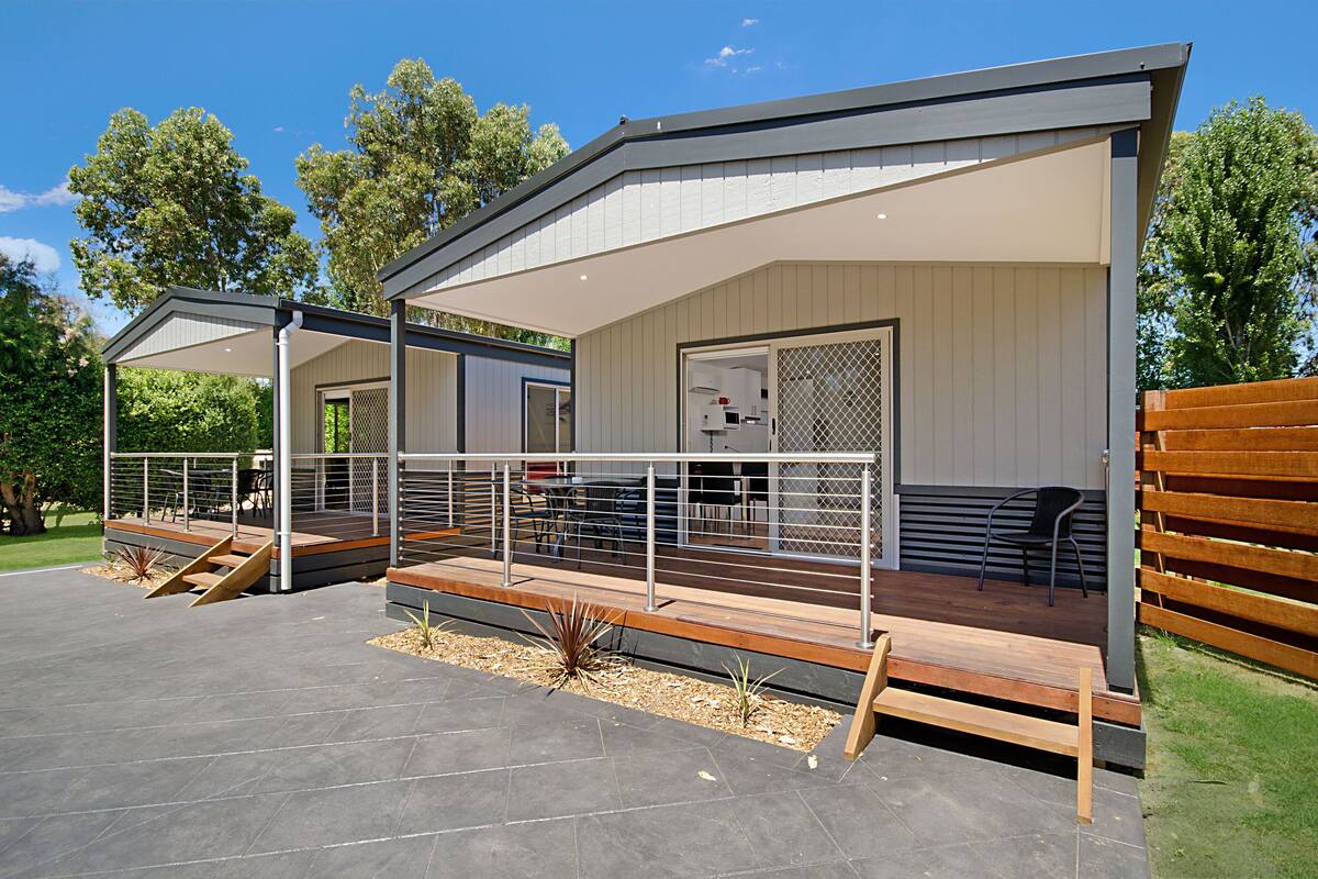 A modern outdoor patio area with a covered seating area, wooden deck, and a small garden.