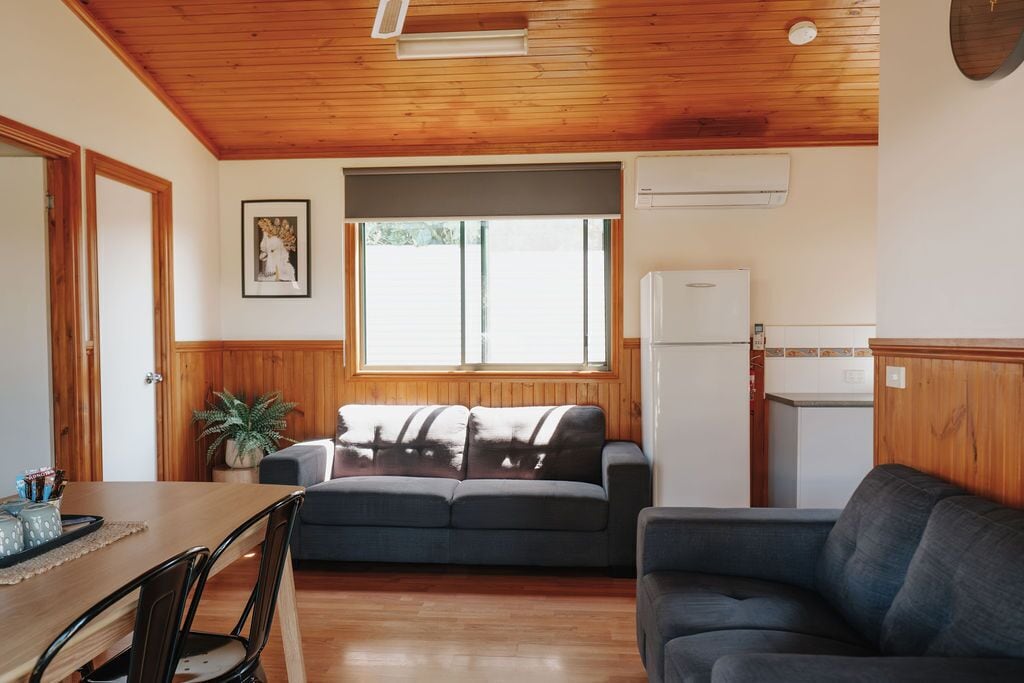 A cozy room with a wooden ceiling, a sofa, a dining table with chairs, and a refrigerator.