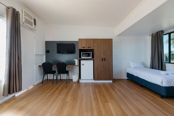 A compact room with a bed, a desk with two chairs, a microwave, and a television.