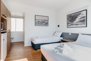 Habitación de hotel con dos camas, microondas, una mesita y ventana. Dos cuadros enmarcados decoran la pared.