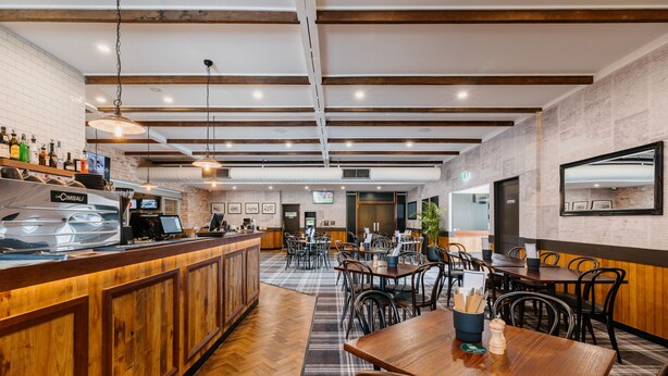 A restaurant with a wooden bar, multiple tables, and chairs. - Boomerang Motor Hotel (West Mackay)