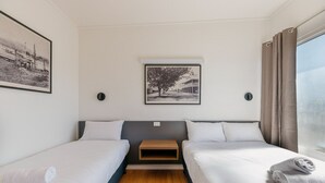 A hotel room with two single beds, a small wooden nightstand, a framed picture on the wall, and a window with curtains. - Boomerang Motor Hotel (West Mackay)