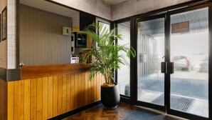 A reception area with a wooden counter, a large potted plant, and a glass door leading outside. - Boomerang Motor Hotel (West Mackay)