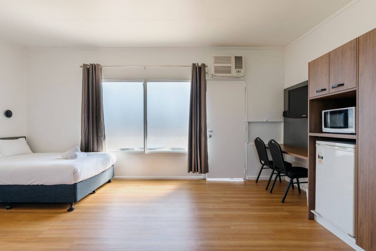A bedroom with a bed, a desk, a chair, a TV, and a microwave.
