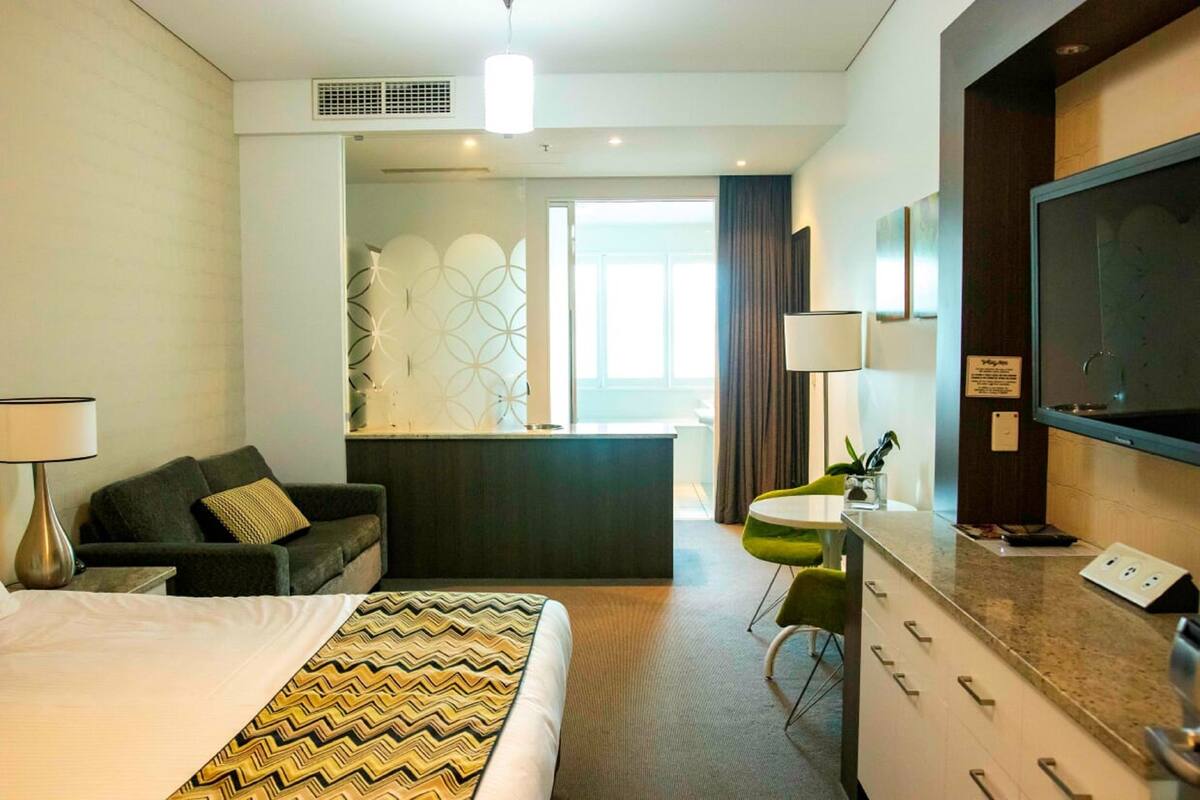 A hotel room with a bed, a desk, a chair, a TV, and a view of the outside.