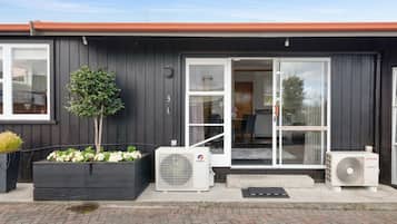 A modern building with a dark exterior, a glass door entrance, and a small garden area with plants.