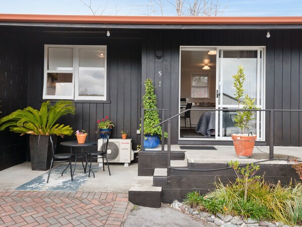 A modern house with a black exterior, a visible number '5' on the door, a small patio with a table and chairs, and potted plants. - Dunrovin Motel (Taupo)