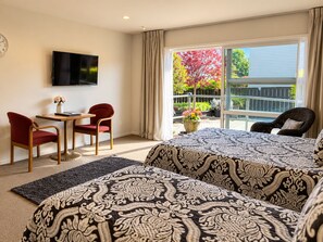 A hotel room with a bed, a desk with a chair, a TV mounted on the wall, and a balcony with a view of trees. - Dunrovin Motel (Taupo)