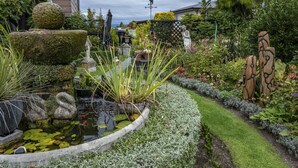 Un jardín con un estanque, esculturas de piedra y diversas plantas.