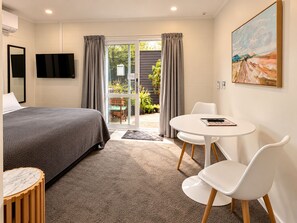A hotel room with a bed, a round table with chairs, a painting on the wall, and a view of the outdoors through a glass door. - Dunrovin Motel (Taupo)