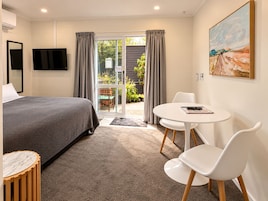 Una habitación de hotel con una cama, una mesa redonda con sillas, un cuadro en la pared y vistas al exterior a través de un ventanal.