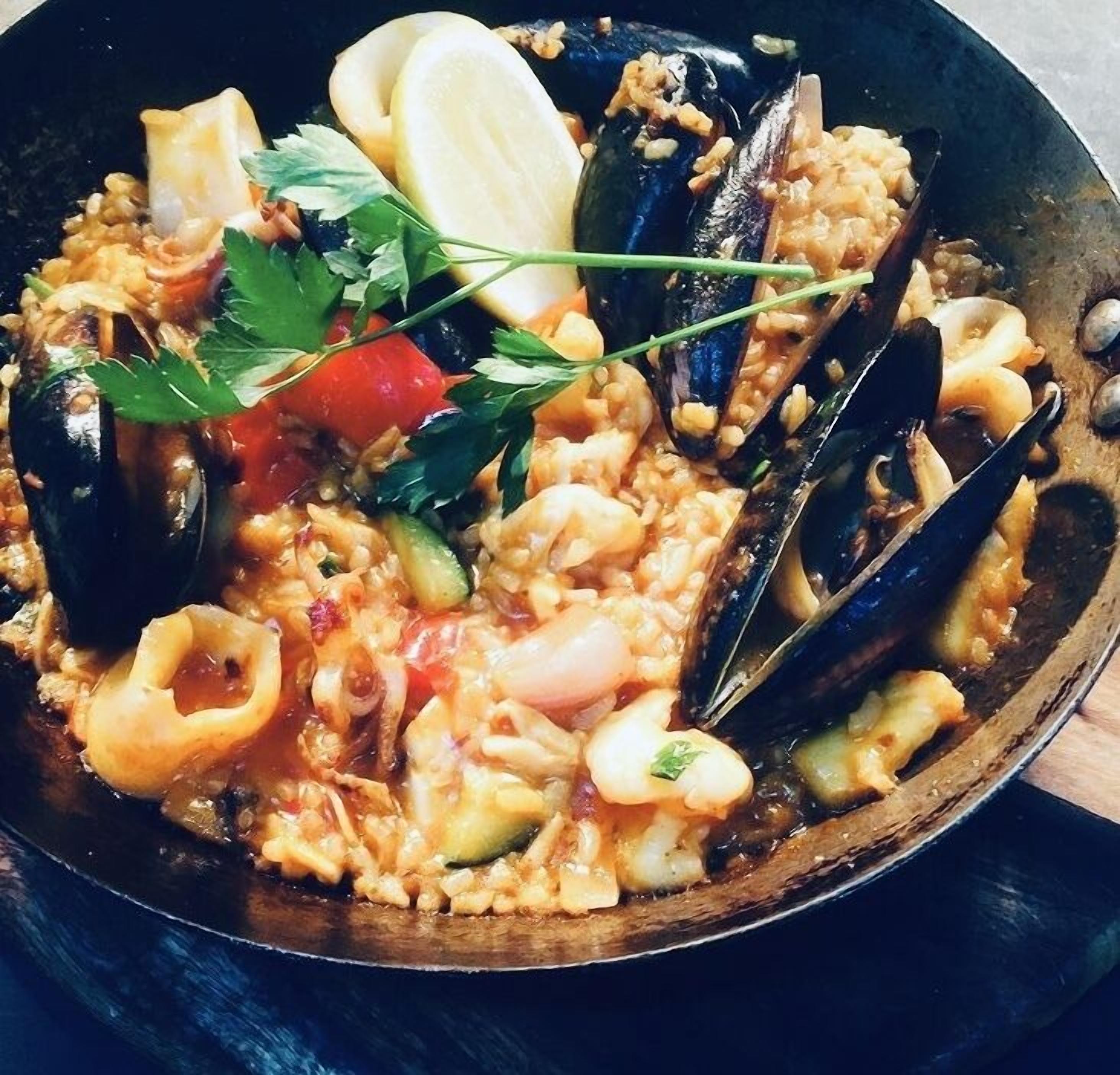 A seafood dish with mussels, squid, and rice, garnished with parsley.