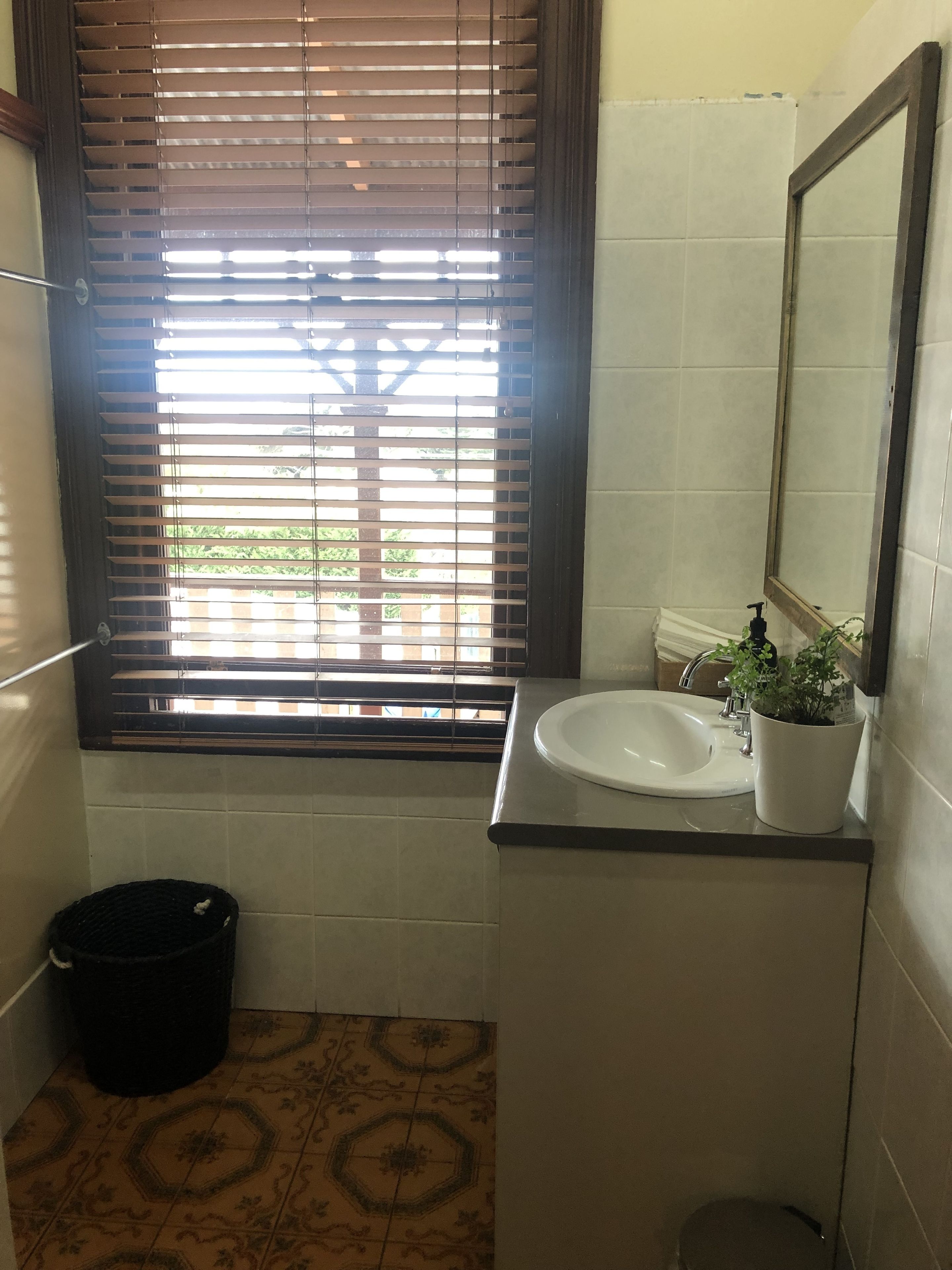 Un baño con ventana, lavamanos, espejo y cubo de basura.