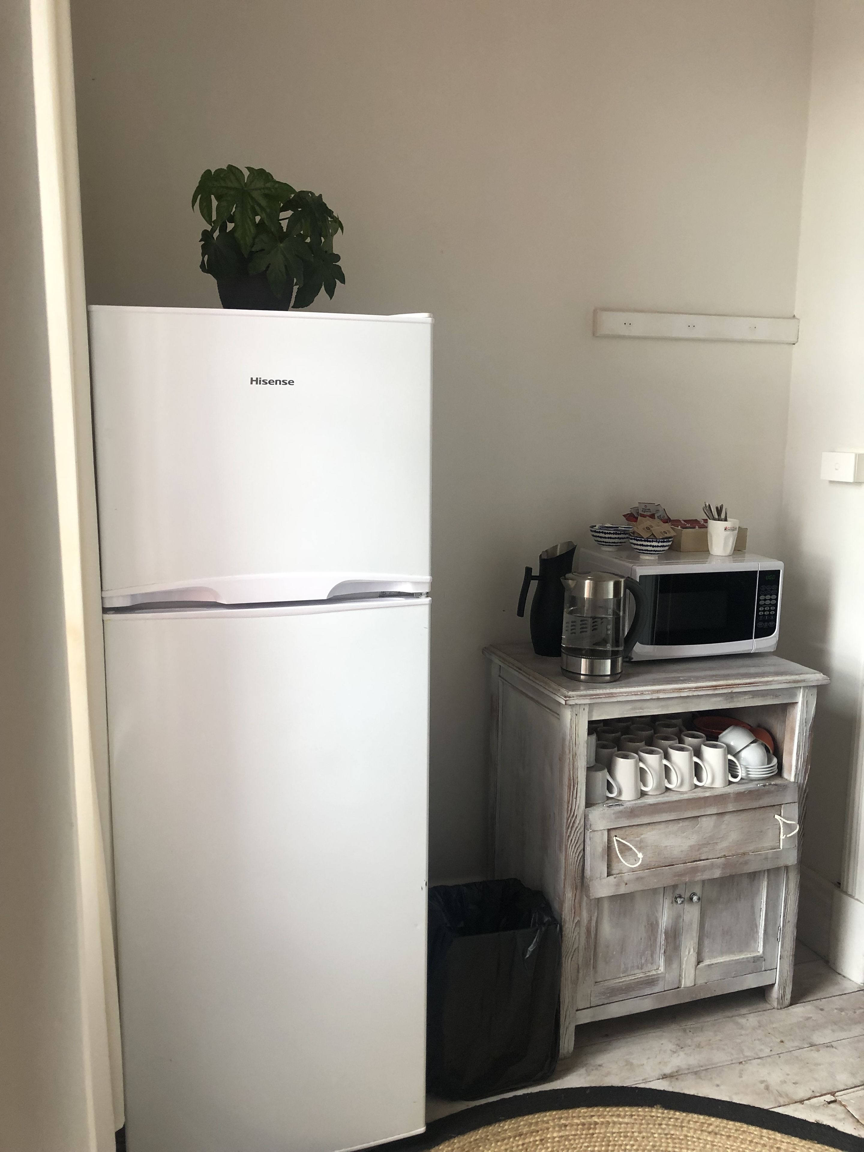 A compact kitchen with a white refrigerator, a microwave, and a small cabinet with mugs and dishes.