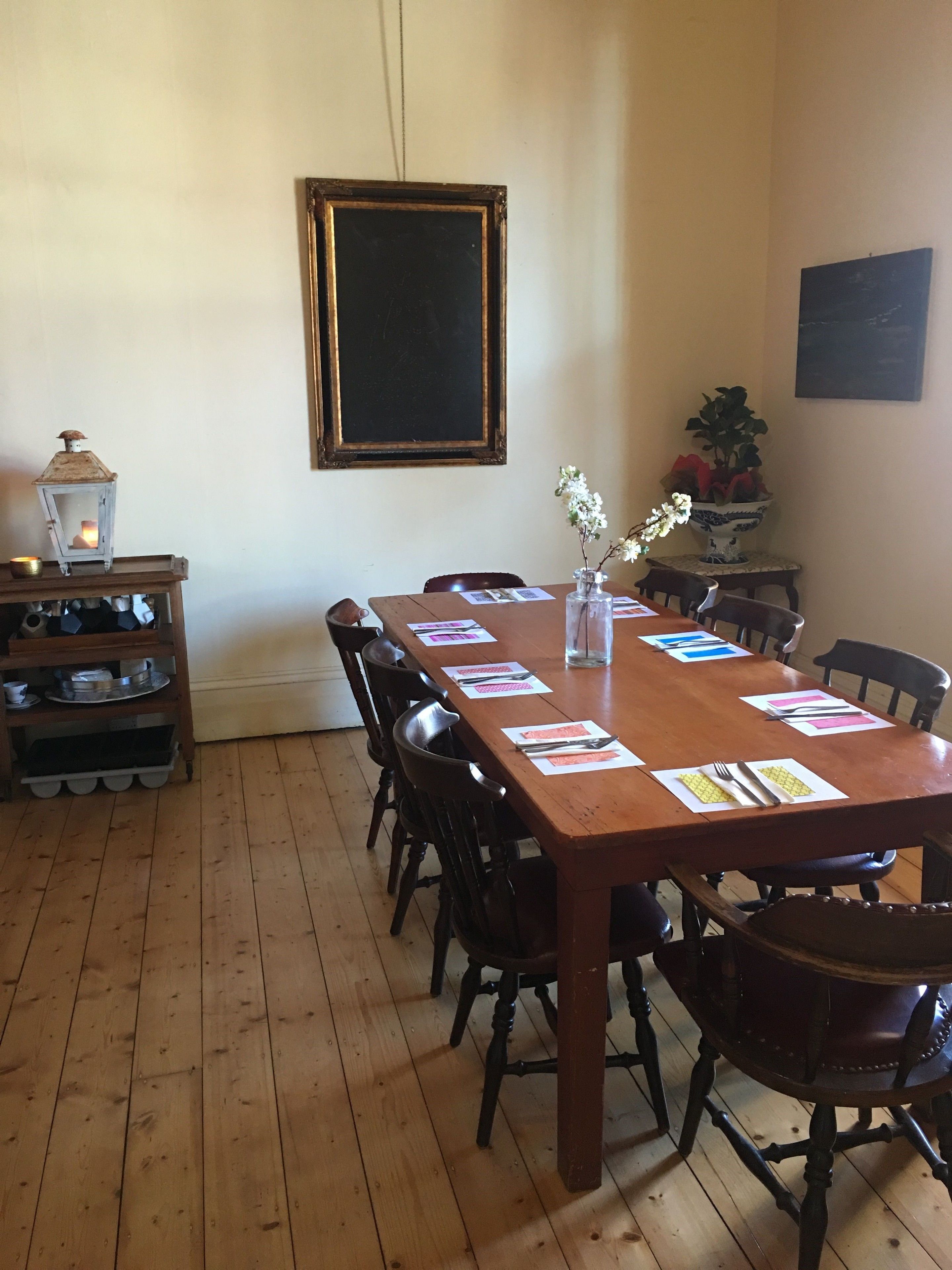 A wooden dining table with chairs, a vase with flowers, a lantern, and a chalkboard on the wall.